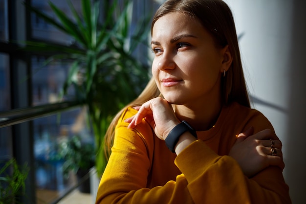 Une fille en pull jaune est assise près d'une grande fenêtre avec un téléphone rouge.