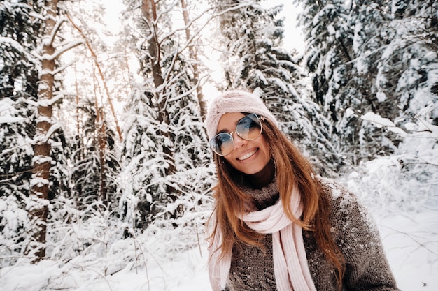 Une fille en pull et lunettes en hiver dans une forêt enneigée