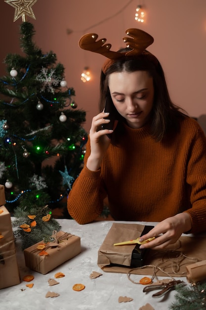 une fille en pull marron tient un téléphone et emballe des cadeaux pour le nouvel an