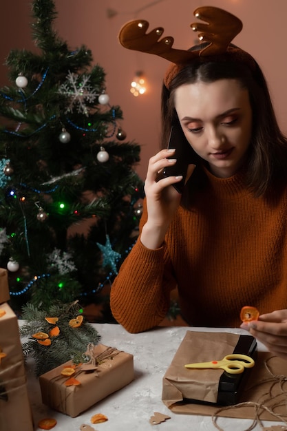 une fille en pull marron tient un téléphone et emballe des cadeaux pour le nouvel an