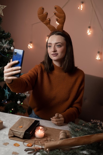une fille en pull marron tient un téléphone et emballe des cadeaux pour le nouvel an
