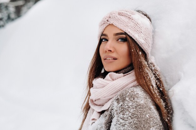 Une fille en pull et mitaines en hiver se dresse sur un fond enneigé.