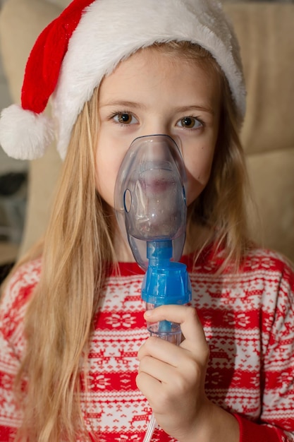 une fille en pyjama du Nouvel An et un chapeau de Père Noël tient un inhalateur dans ses mains