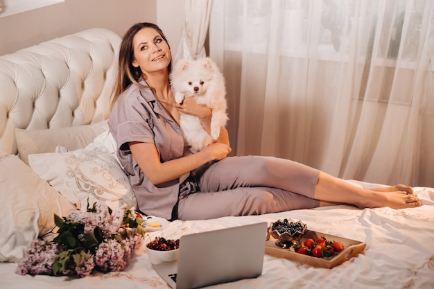 Une fille en pyjama est assise dans son lit la nuit avec son chien blanc