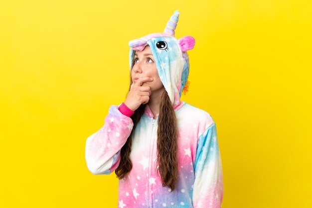 Fille avec un pyjama de licorne sur fond isolé ayant des doutes et avec une expression de visage confuse