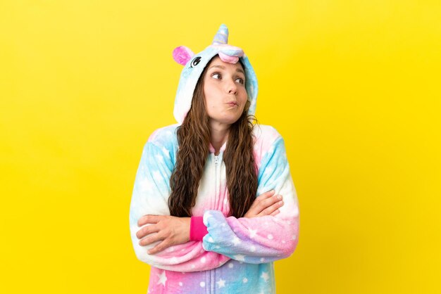 Fille avec pyjama licorne sur fond isolé faisant des doutes geste tout en soulevant les épaules