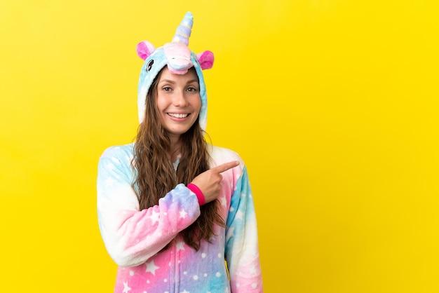 Fille avec pyjama licorne sur fond isolé pointant vers le côté pour présenter un produit