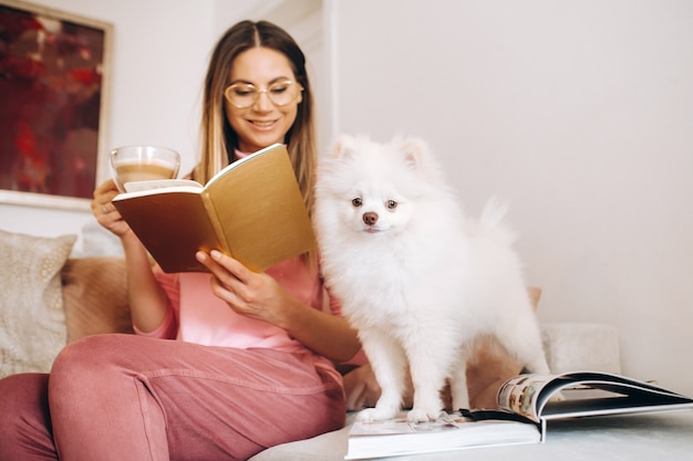 Une fille en pyjama à la maison lit un livre avec son chien