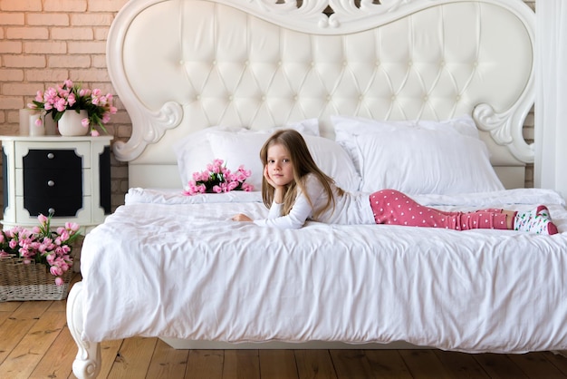 fille en pyjama se trouve sur un lit avec des draps blancs. Décor fleuri.