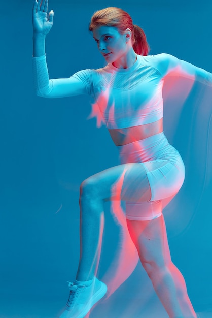 Fille qui court en uniforme de sport blanc sur fond bleu modèle de sport isolé en studio avec lumière