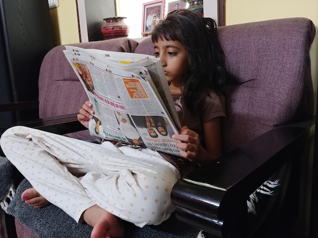 Photo une fille qui lit un journal assise sur une chaise à la maison.