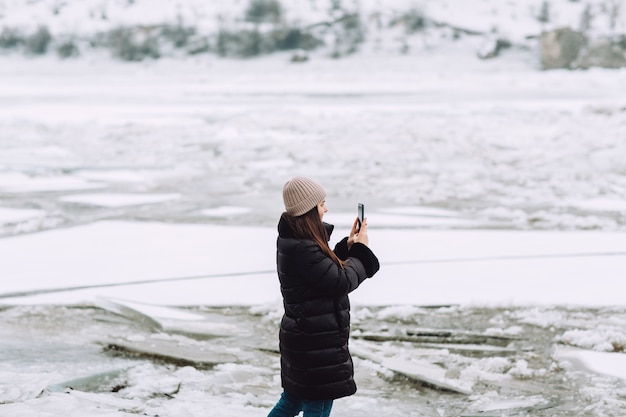 Fille qui marche en plein air et prendre des photos sur téléphone mobile la rivière gelée.