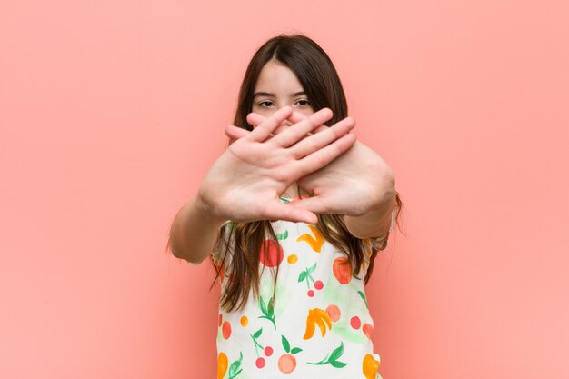 Fille qui porte un vêtement d'été contre un mur rouge, faisant un geste de déni