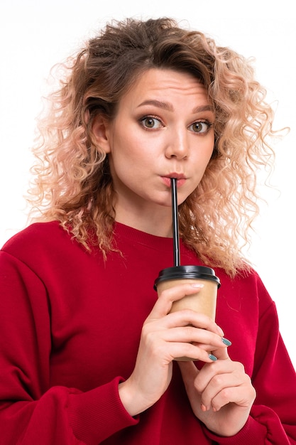 Fille de race blanche aux cheveux blonds bouclés boit du café et des sourires, portrait isolé