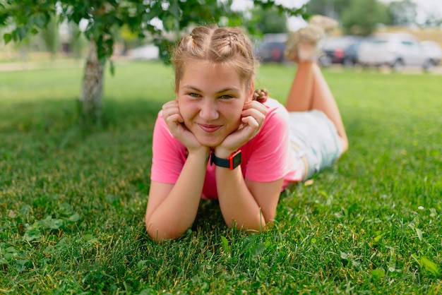 Fille de race blanche avec des taches de rousseur et dans un T-shirt rose se trouve sur l'herbe. Une étudiante sourit et profite du beau temps d'été.