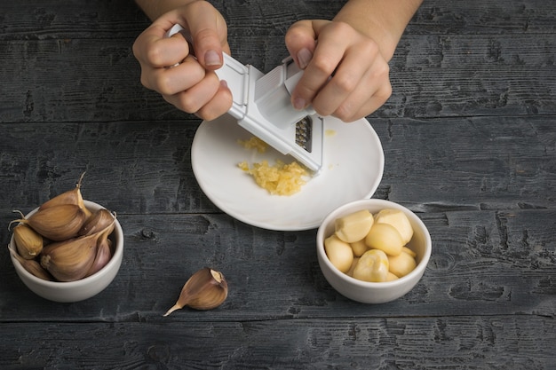 Une fille râpe l'ail sur une râpe sur une table en bois. Une épice populaire pour la cuisine.