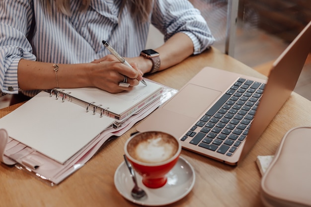 La fille recadrée travaille, prend des notes dans le planificateur.