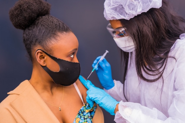 Fille recevant l'injection du vaccin contre le coronavirus par un médecin noir