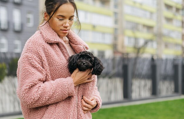 Une fille réchauffe un petit chiot bouclé sous son manteau par une fraîche journée de printemps