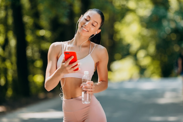 Fille regardant l'écran sur smartphone et écouter de la musique dans les écouteurs en plein air.