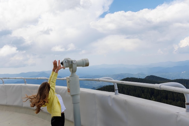 Fille regardant des paysages de Rhodopes et ciel nuageux à travers le télescope sur la tour d'observation en haut Snezhana