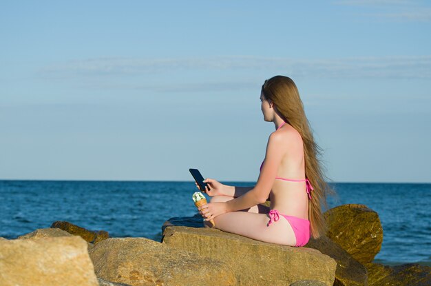 Fille regardant pensivement dans le téléphone, en maillot de bain sur la plage