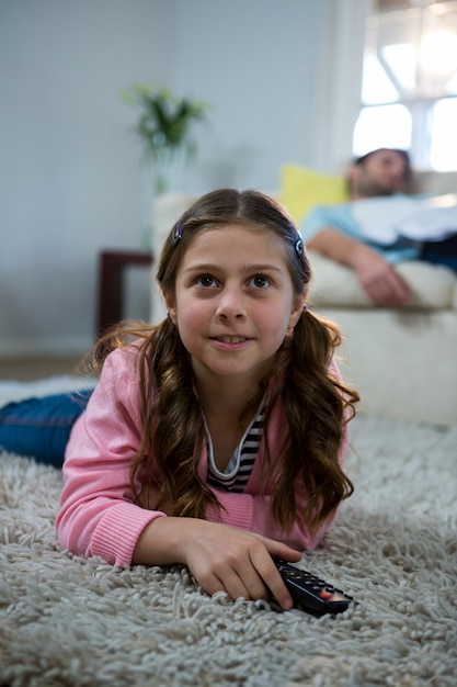 Fille regardant la télévision allongé sur le tapis dans le salon