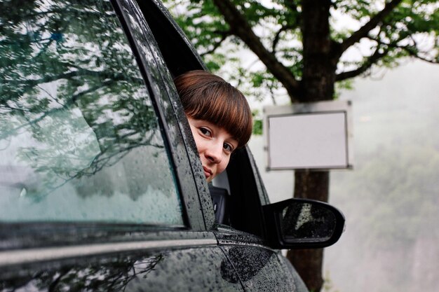 fille regarde par la fenêtre de la voiture par temps de pluie lors d'un road trip