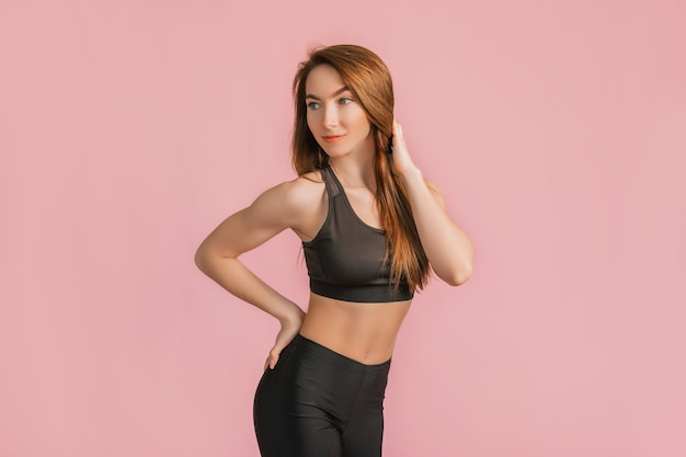 Fille de remise en forme souriante en vêtements de sport noirs sur une surface rose