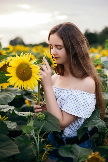 La fille renifle le bouquet jaune du champ de tournesol de floraison