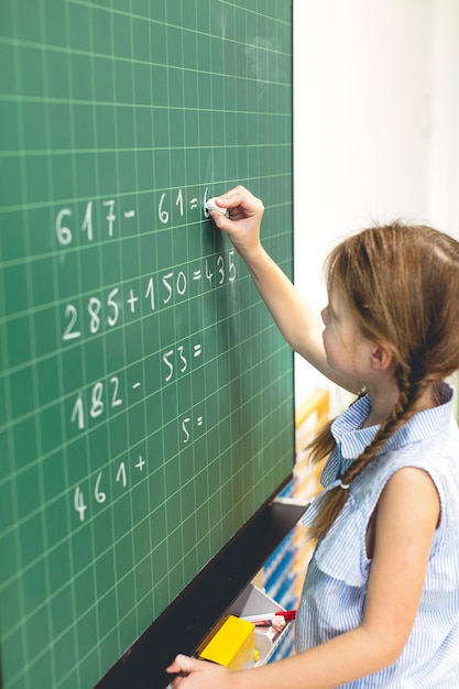 Une fille résout une équation mathématique sur un tableau noir en classe à l'école.