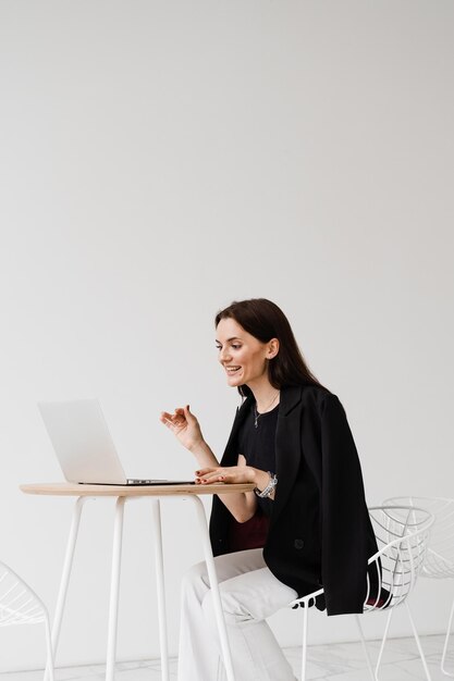 Une fille responsable avec un ordinateur portable gesticule discute des tendances et des tâches dans un bureau blanc Réunion vidéo en ligne avec des collègues et des partenaires commerciaux Discussion d'équipe et résolution de problèmes à distance