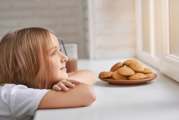 Fille rêveuse avec des cookies sur le rebord de la fenêtre