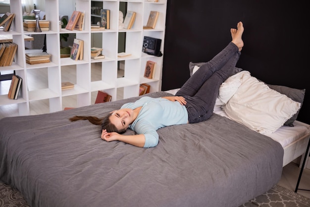 une fille rêveuse dans un pull et un jean se trouve sur le lit dans la chambre et regarde ailleurs