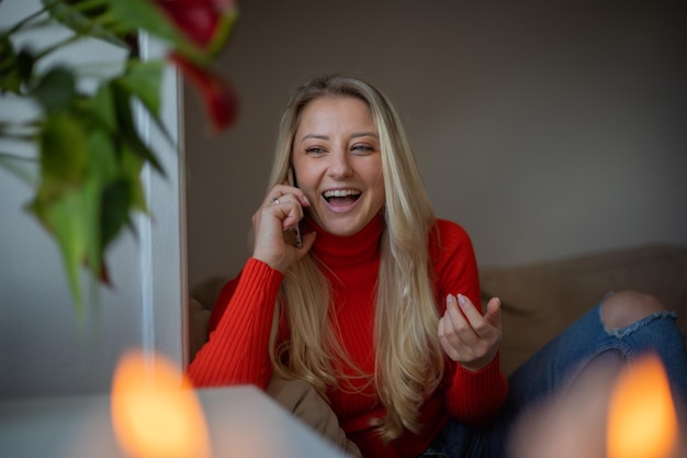 Une fille rit en parlant au téléphone à la maison assise sur son concept de bonheur de canapé