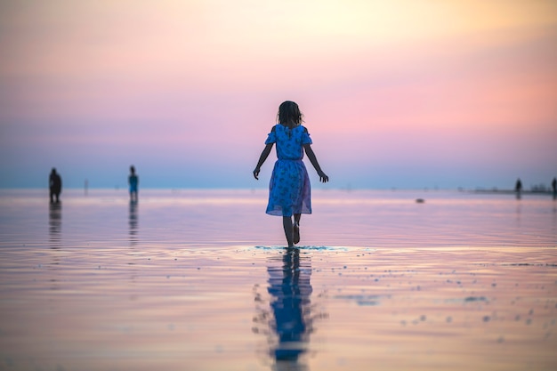 Une fille en robe au bord de la mer au coucher du soleil marche sur l'eau