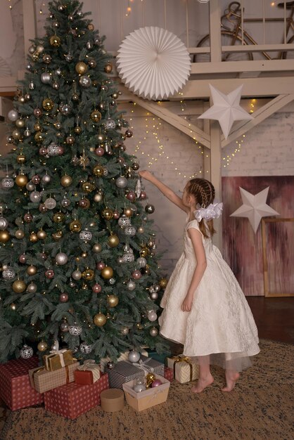 Une fille en robe blanche décore le sapin de Noël