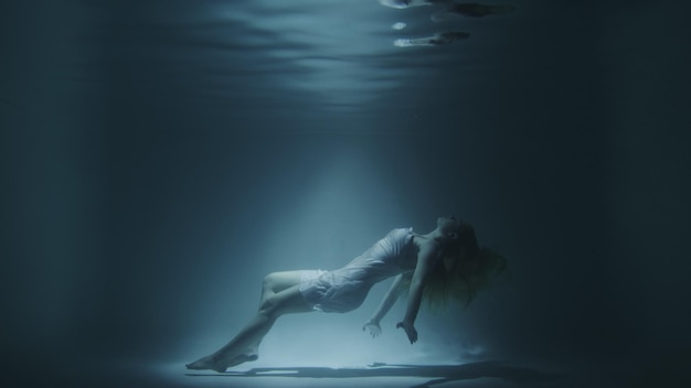 Une fille en robe blanche nage sous l'eau