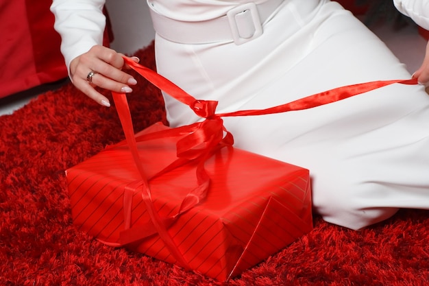 Une fille en robe blanche ouvre une boîte rouge avec des cadeaux.