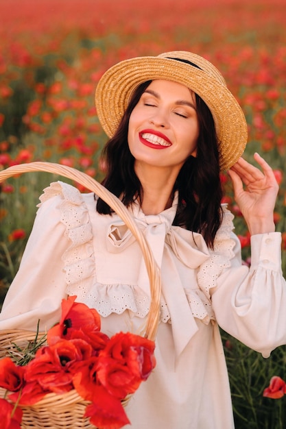 Une fille en robe blanche et avec un panier de coquelicots se promène dans un champ de coquelicots