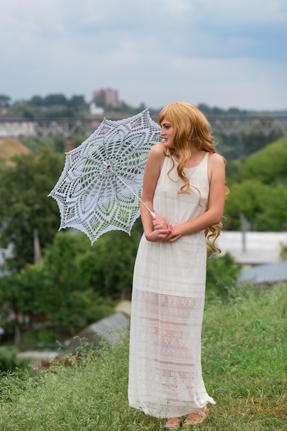 Une fille en robe blanche avec parasol blanc posant sur fond de ville.