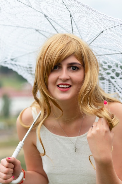 Une fille en robe blanche avec parasol blanc posant sur fond de ville.