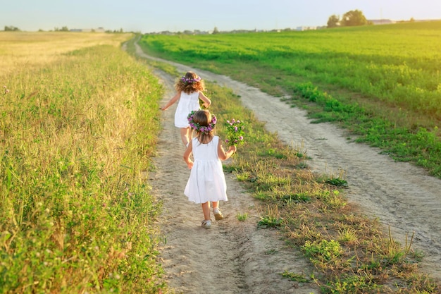 Fille en robe blanche rattrape sa soeur qui court le long d'une route sablonneuse dans un champ