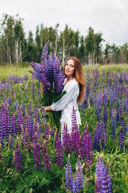 Une fille en robe blanche se tient parmi les lupins