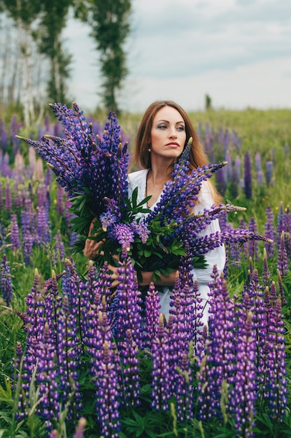 Une fille en robe blanche se tient parmi les lupins