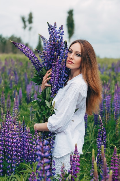 Une fille en robe blanche se tient parmi les lupins