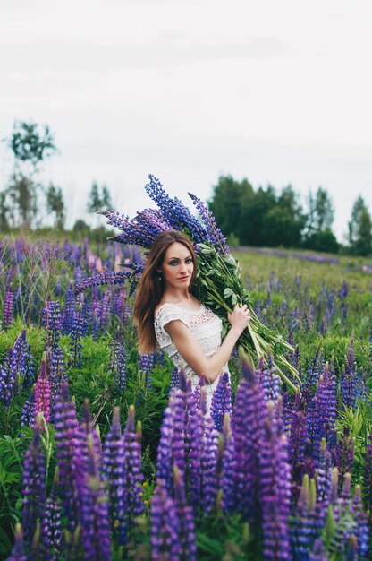 Une fille en robe blanche se tient parmi les lupins