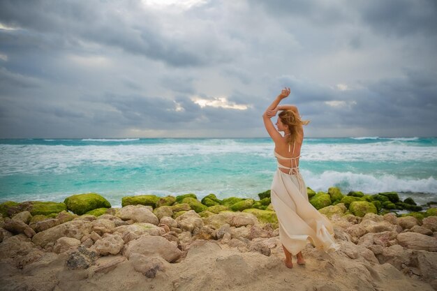 Une fille en robe blanche se tient sur le rivage de la mer des Caraïbes de la plage de Cancun