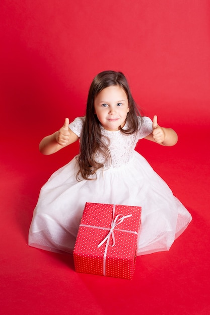 Une fille en robe blanche sourit, montre un pouce en l'air.