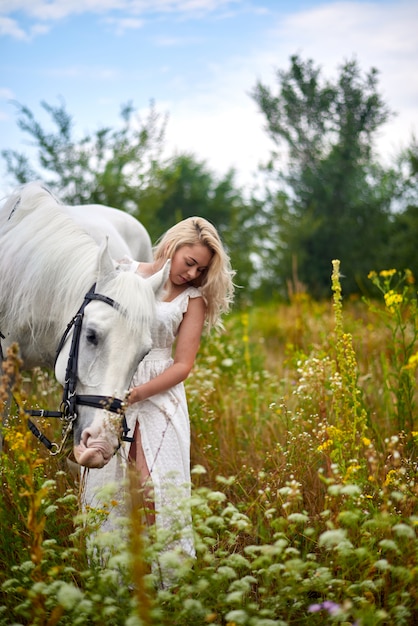 Fille en robe blanche tenant un cheval dans le champ